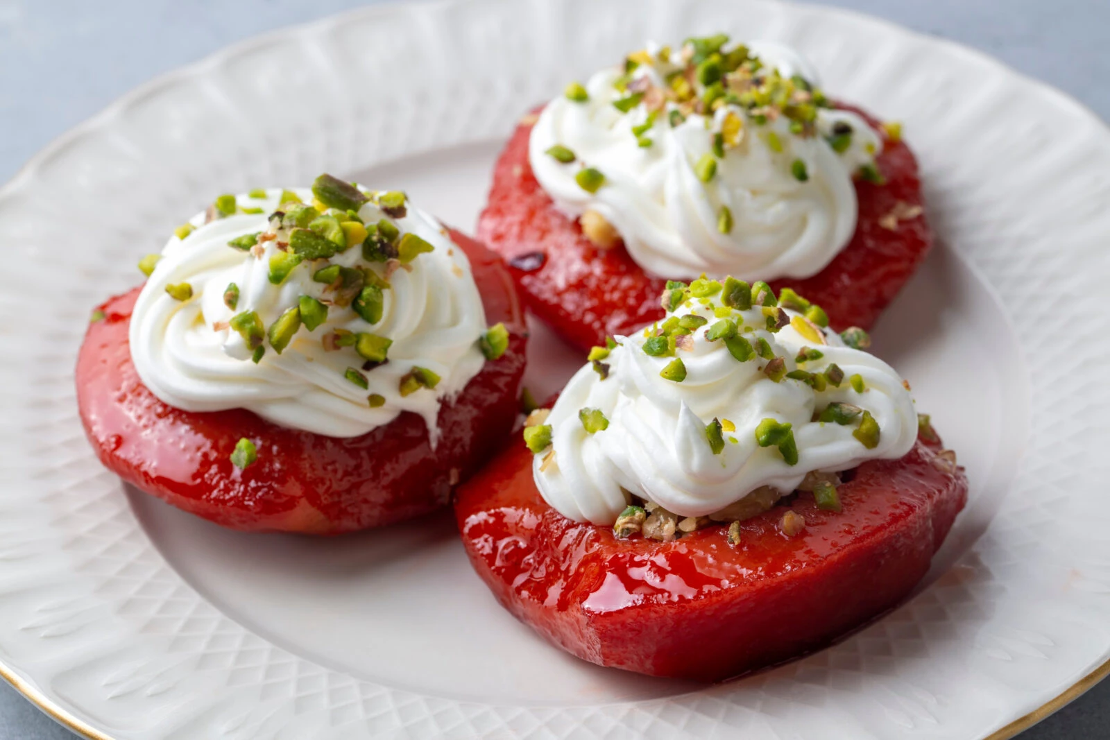 A plate of firinda ayva tatlisi, baked quince dessert with honey, walnuts, and whipped cream, garnished with finely chopped pistachios.