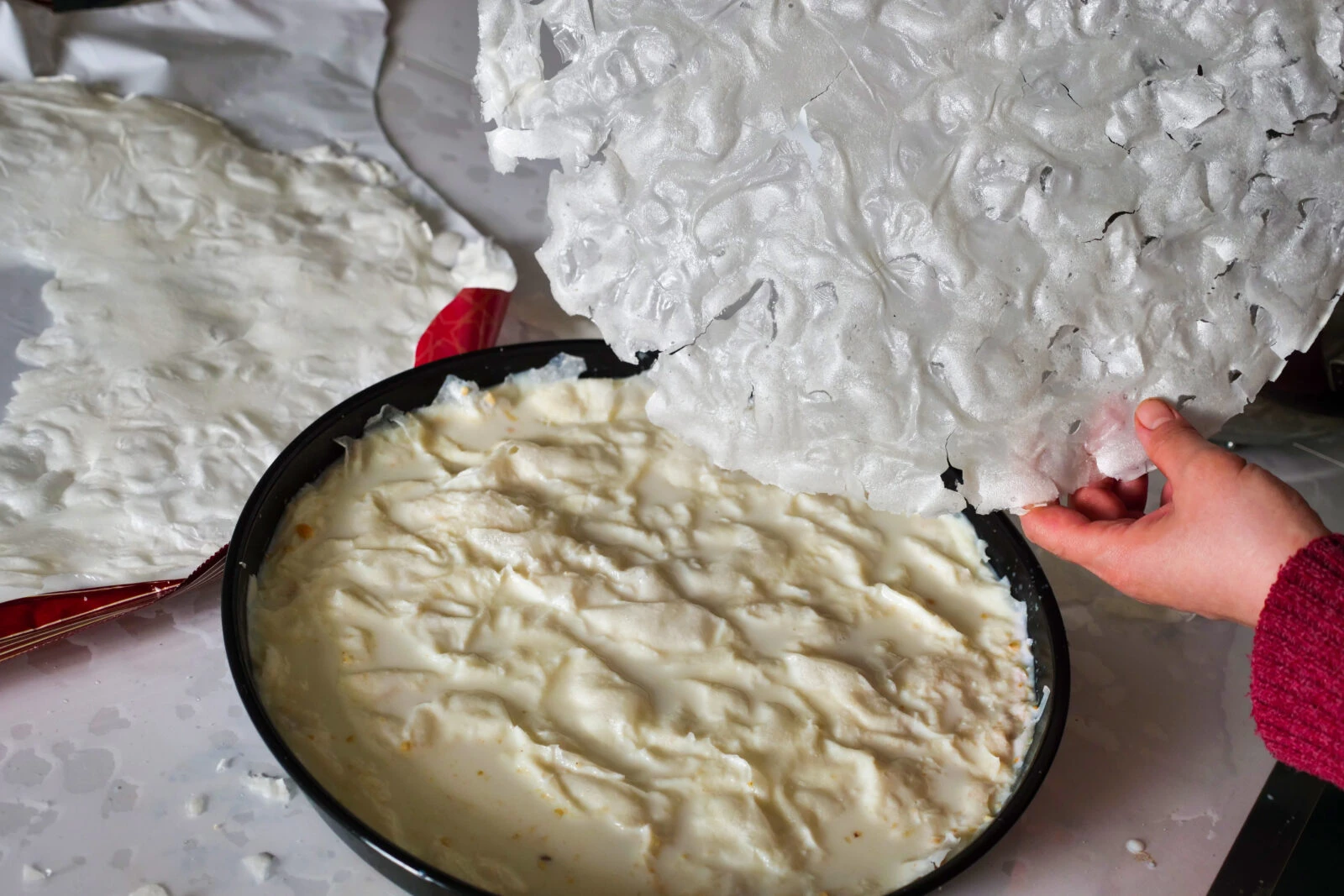 A woman preparing gullac with varak sheets resembling dough.