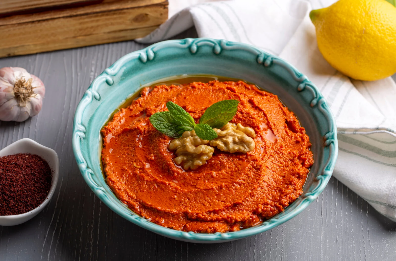 A bowl of Muhammara, a Turkish and Middle Eastern dip made with walnuts, roasted red peppers, and spices, garnished with mint and walnuts.