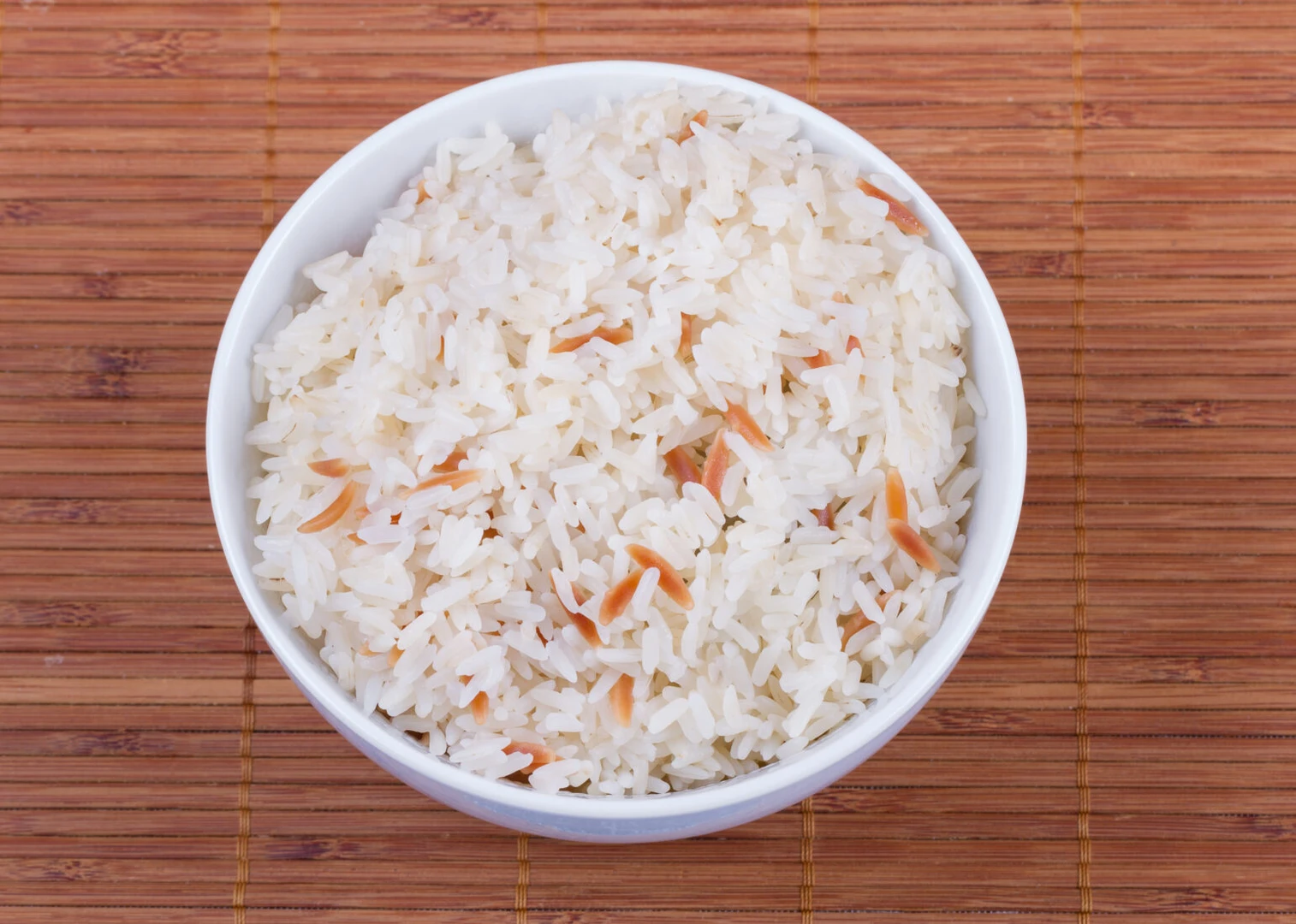 A close-up of a bowl of Turkish recipe rice pilaf, prepared with long-grain rice and toasted vermicelli, served on a wooden mat.