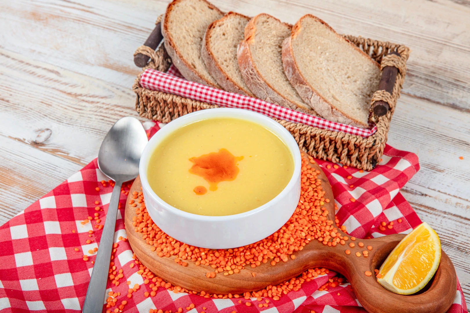 A bowl of Turkish red lentil soup, garnished with red pepper oil and served with rustic bread and lemon wedges on the side.