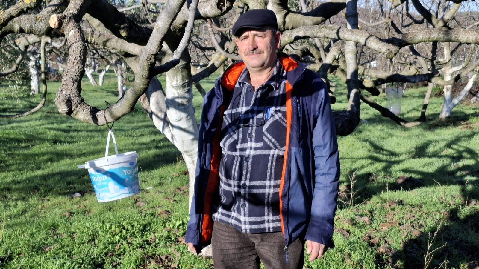 Erkan Firtina, a black fig producer in Bursa, Türkiye, standing in an orchard with fig trees in the background.