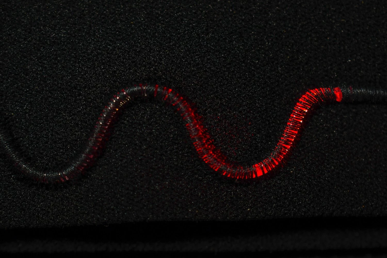 A close-up of a fiber-optic sensor from Llume, glowing red as it runs through a black fabric background.