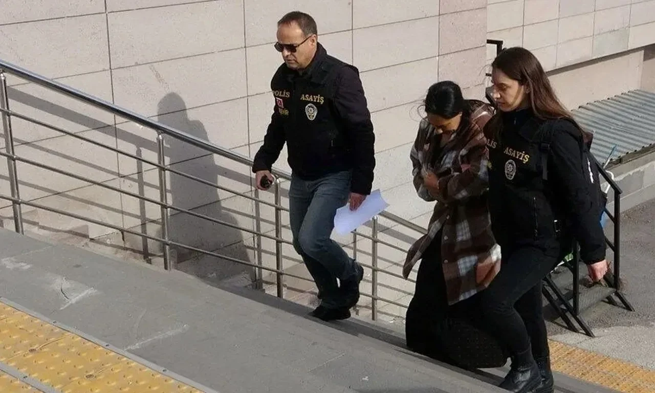 Two police officers escort a woman in a plaid coat up the stairs to a government building.