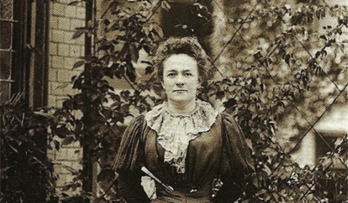 International Women Day - Clara Zetkin in 1897, standing outdoors in a dark dress with lace details, known for her contributions to women's rights and the establishment of International Women's Day.