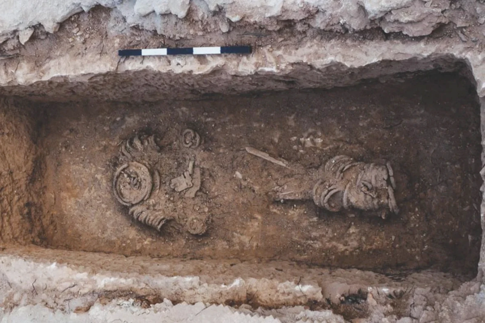 A photograph of an excavated burial site containing the remains of a Byzantine-era individual buried in chains. The skeletal remains, partially preserved, are surrounded by compact soil within a rectangular tomb.