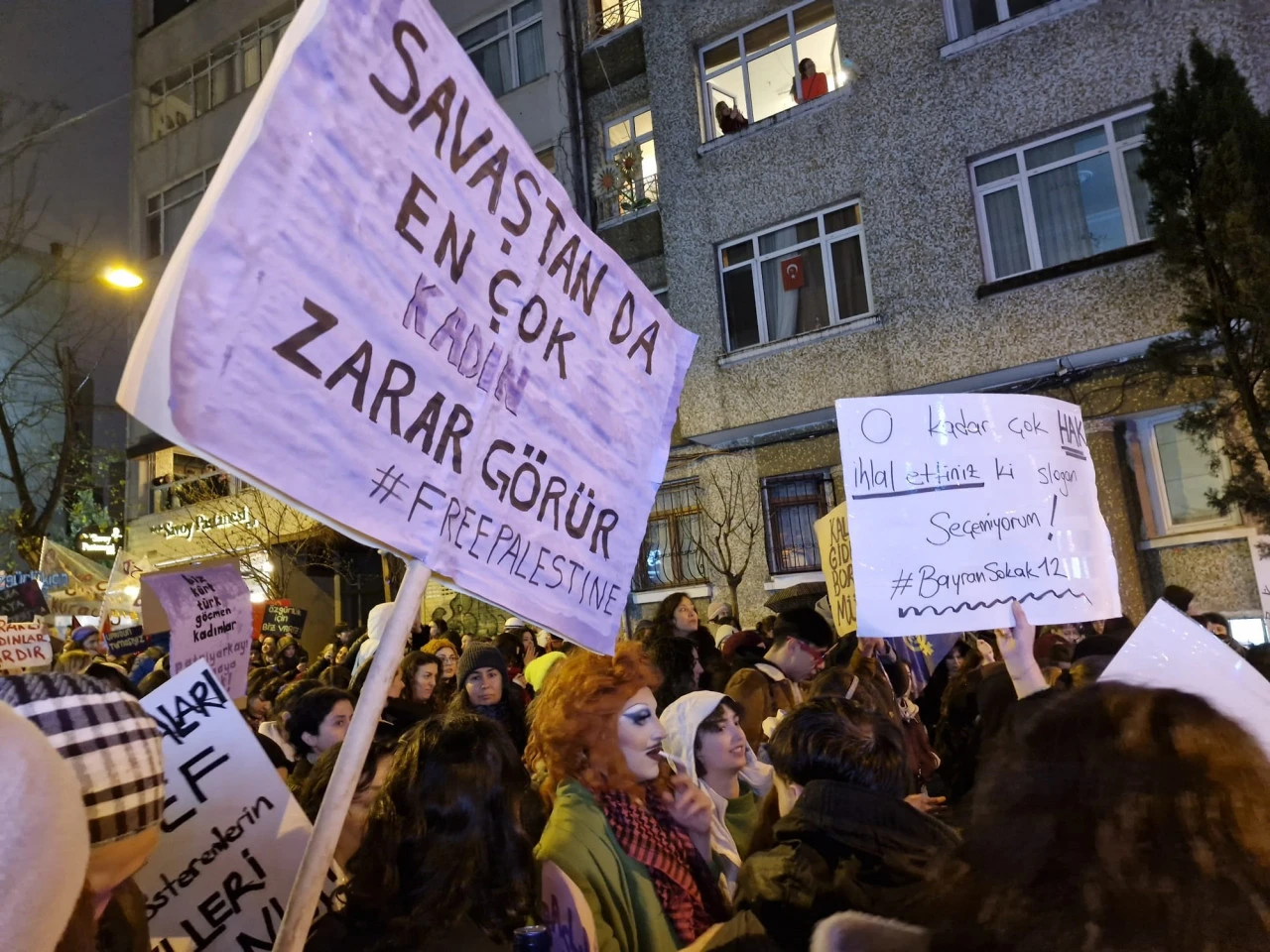 A woman holds a banner at the Feminist Night March, highlighting the disproportionate impact of war on women and showing solidarity with Palestine."