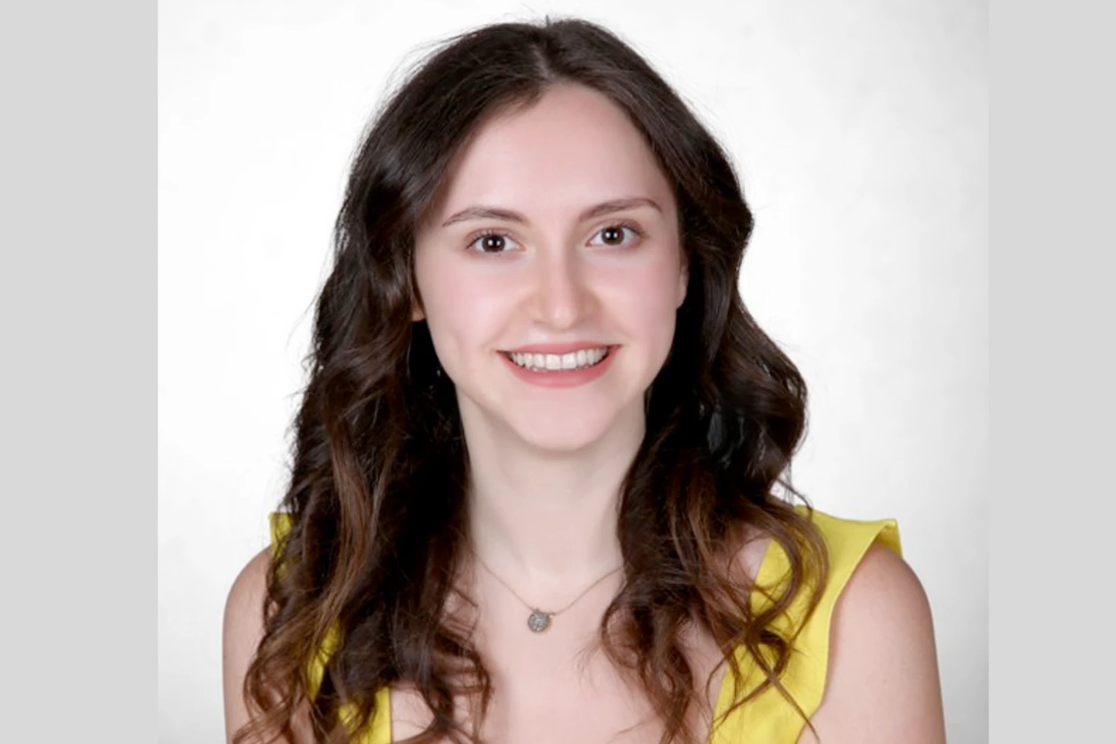 A portrait of Ilayda Samilgil wearing a yellow dress, smiling at the camera with a white background.