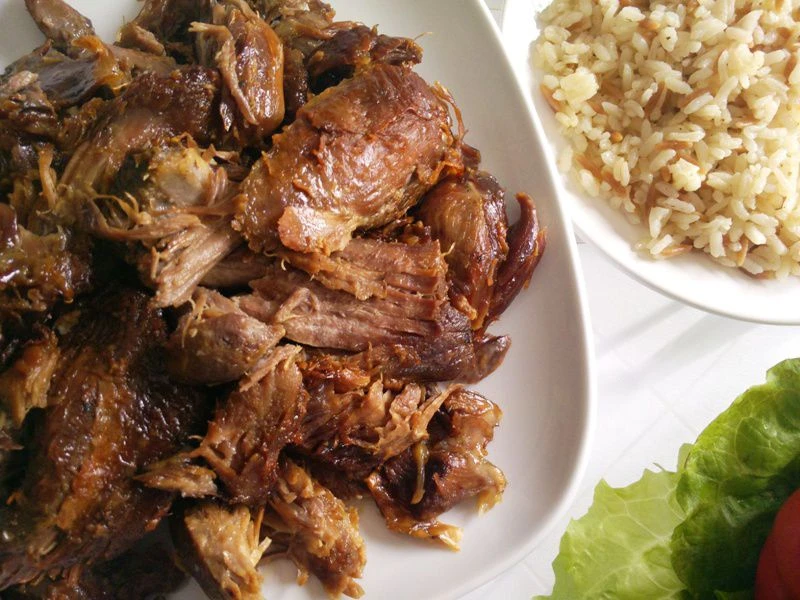 A plate of shredded kuzu tandir, Turkish-style slow-cooked lamb shoulder, served with a side of rice pilaf.