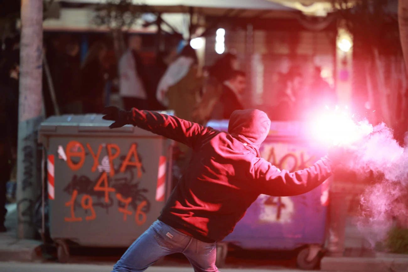 A hooded protester throws a flare during clashes with police in demonstrations over the Tempi train disaster, Thessaloniki, Greece, Mar. 5, 2025. (Courtesy of in.gr)