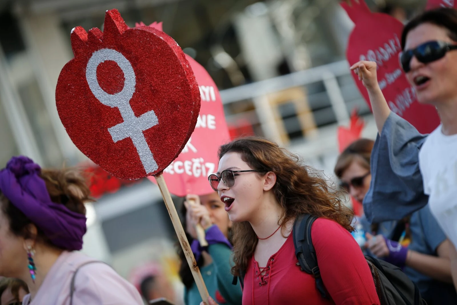 Woman at international women's day protest with red shirt holds up red sign with female gender